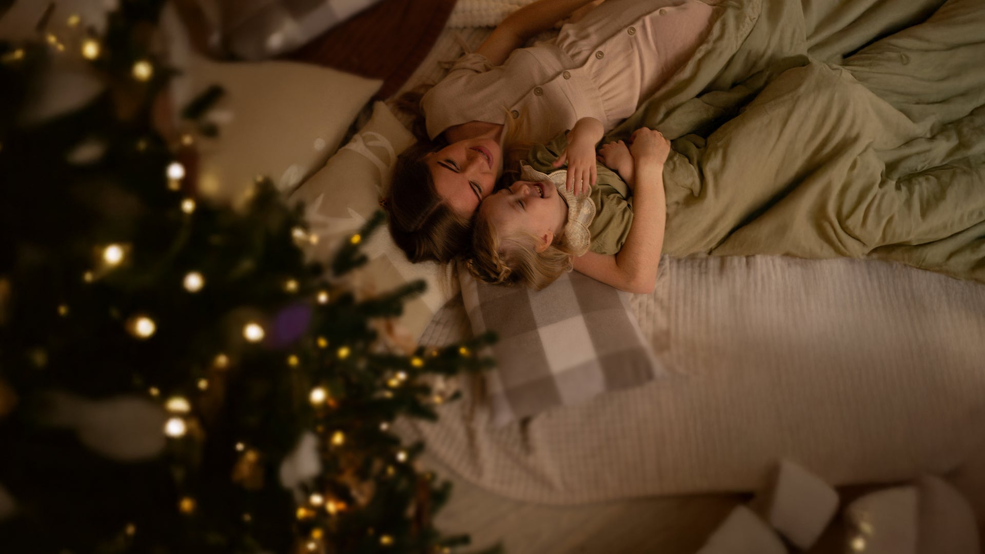 Mother and daughter lying on a bed next to a decorated Christmas tree